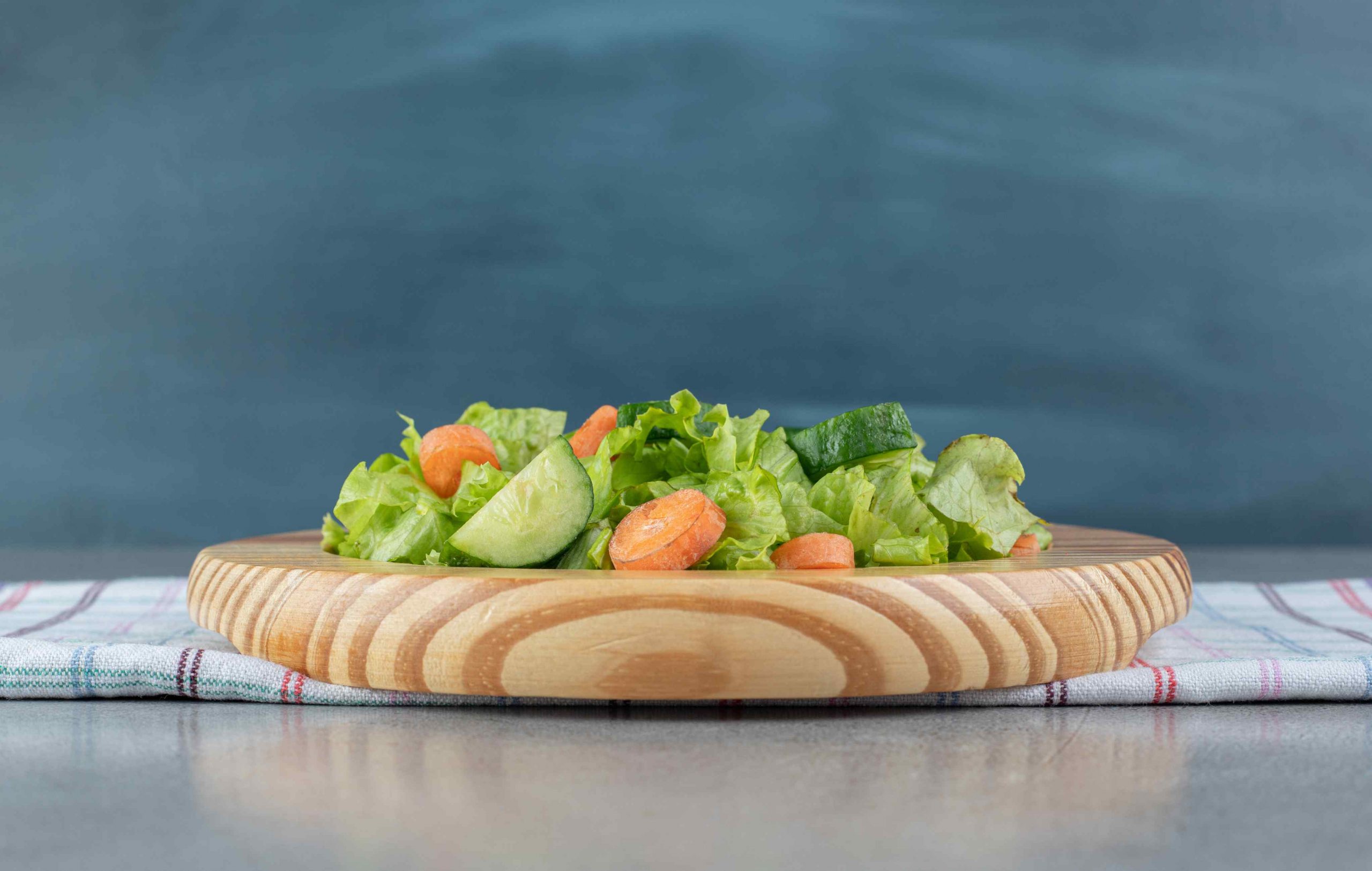 A wooden board with vegetable salad on a tablecloth . High quality photo